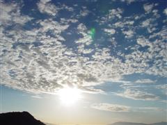 A photo of the sky, with the sun peeking through the clouds, and a mountain just visible on the bottom